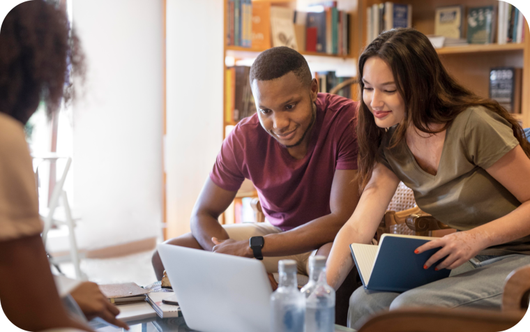 Dos estudiantes sonríen mientras revisan una laptop y un cuaderno